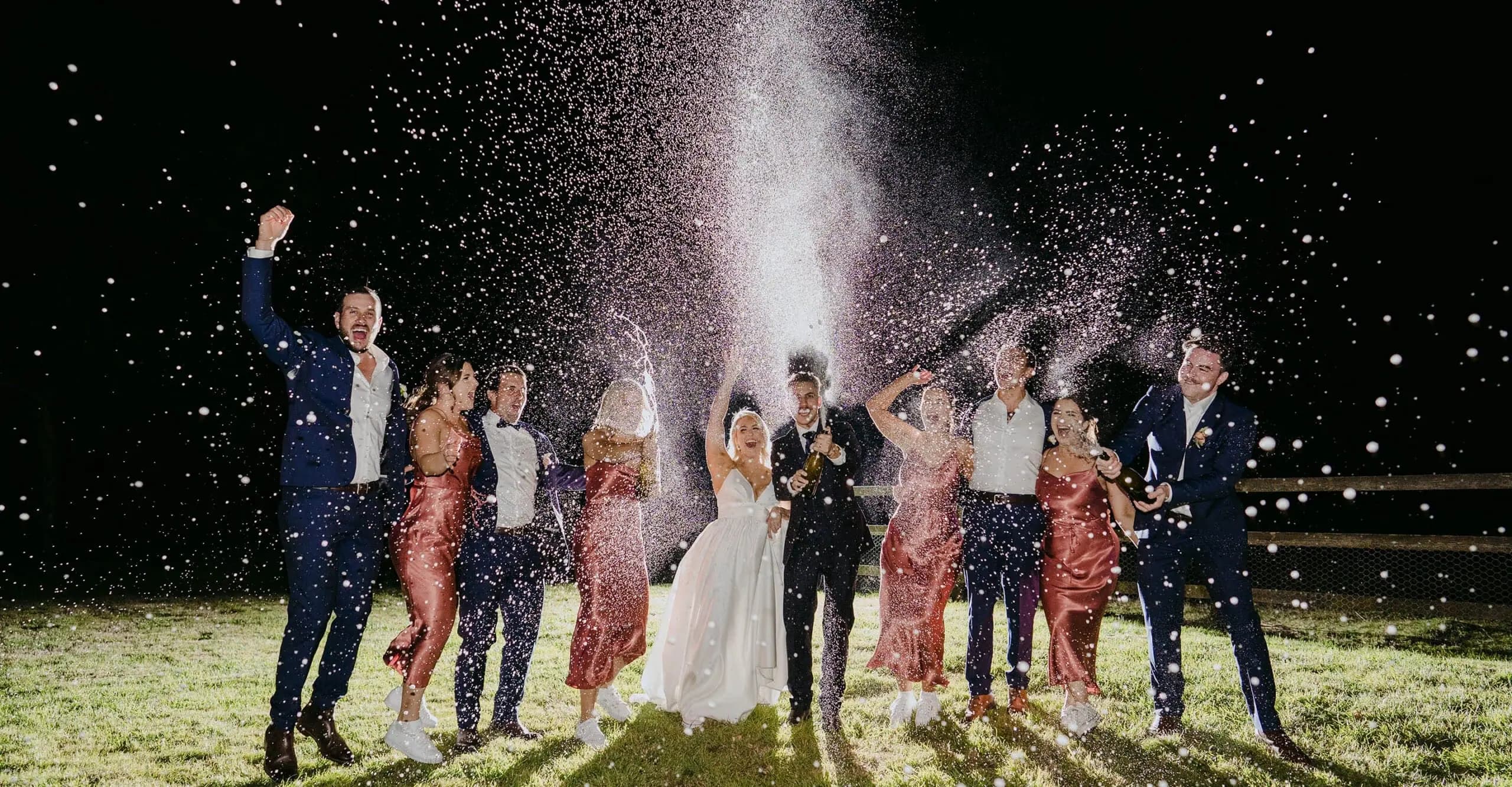 Wedding party celebrating beneath a spray of sparkling wine at night