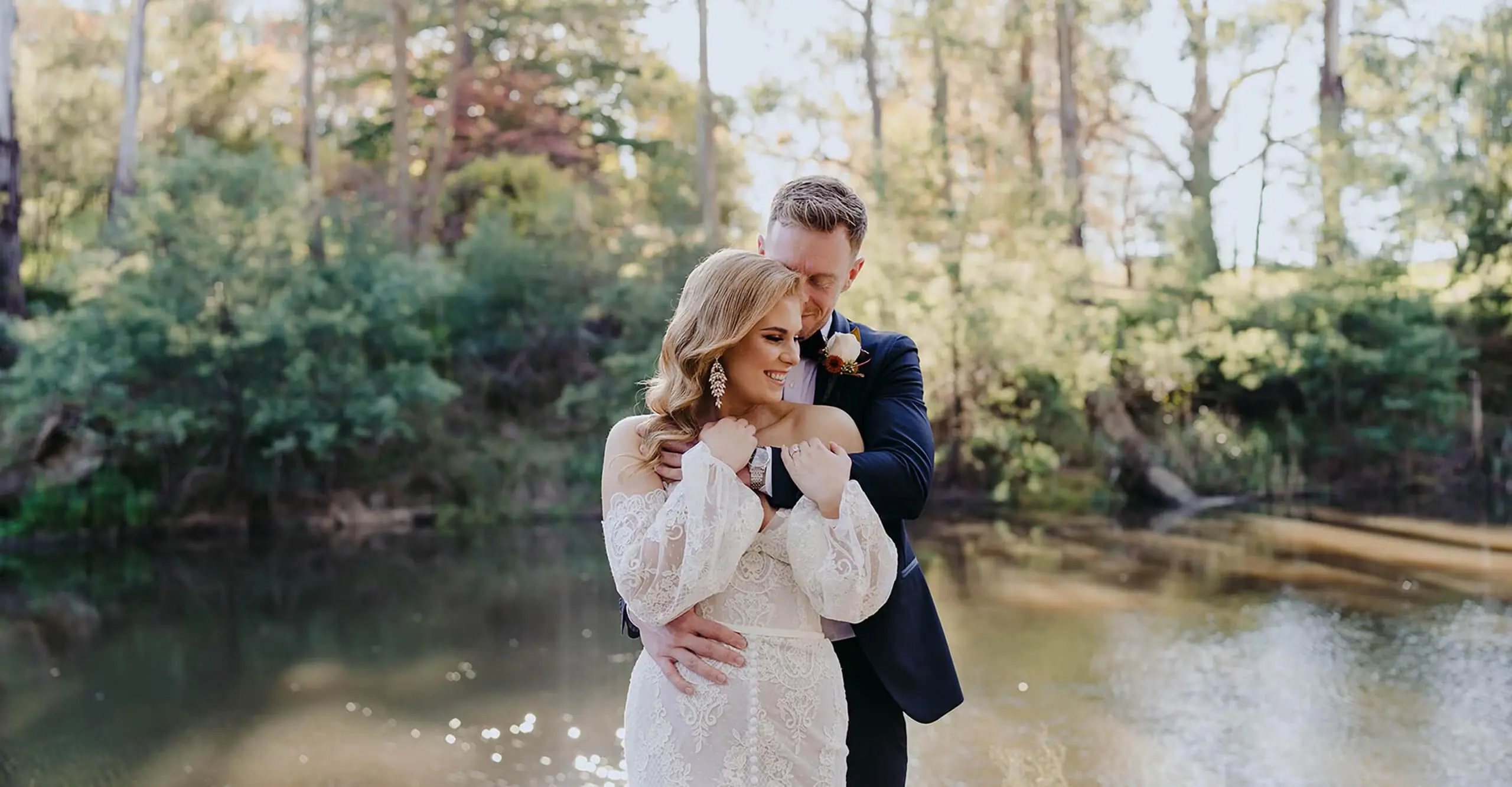 Groom kissing the bride's head beside a pond