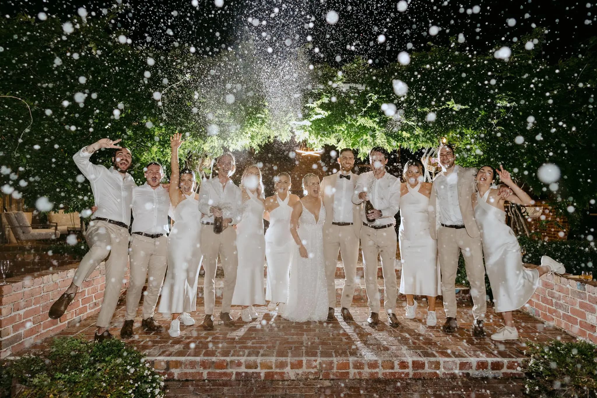 Wedding party laughing beneath a spray of sparkling wine at night.
