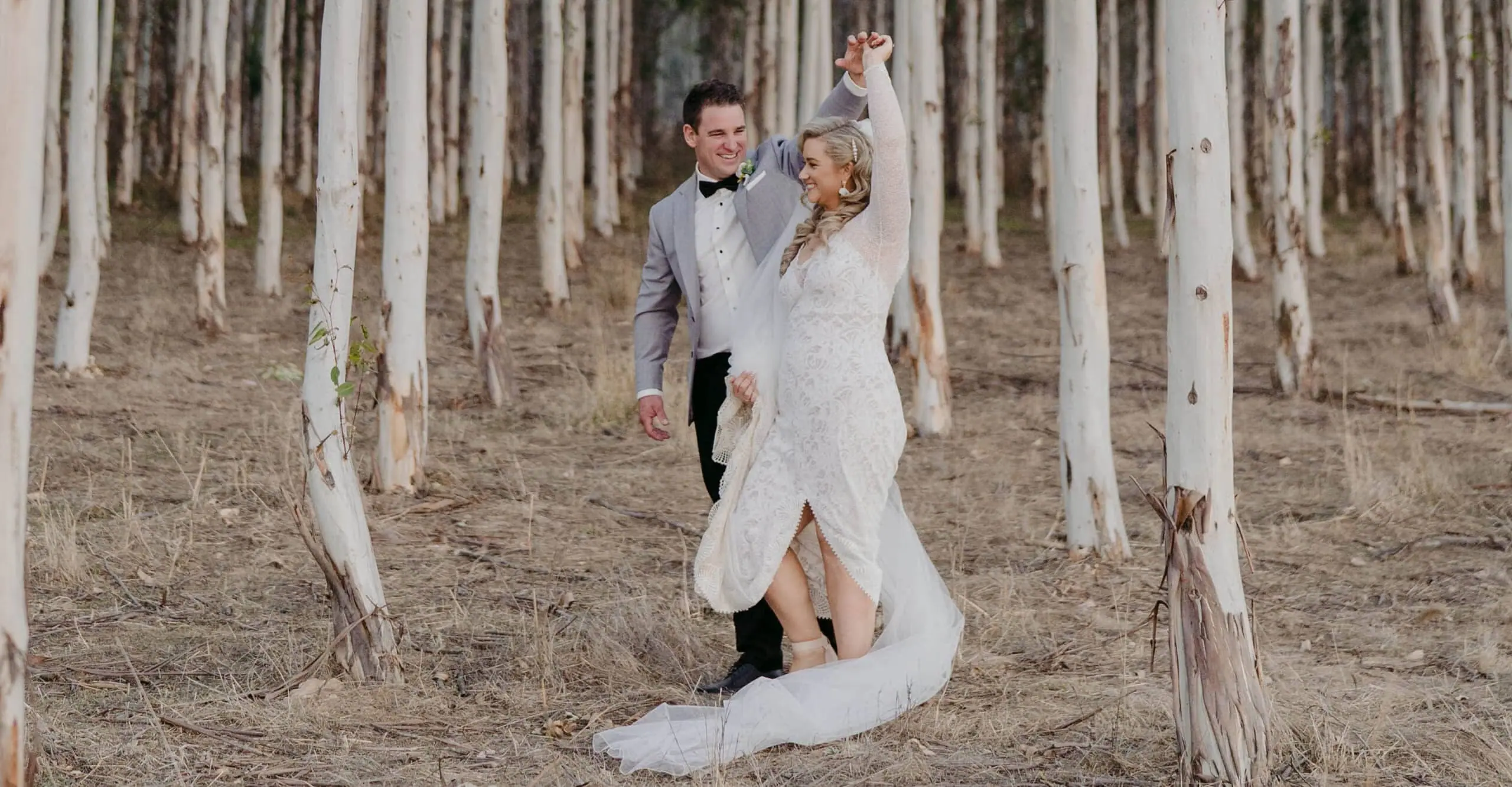 Bride lifting her arm as the couple walk through the woodland
