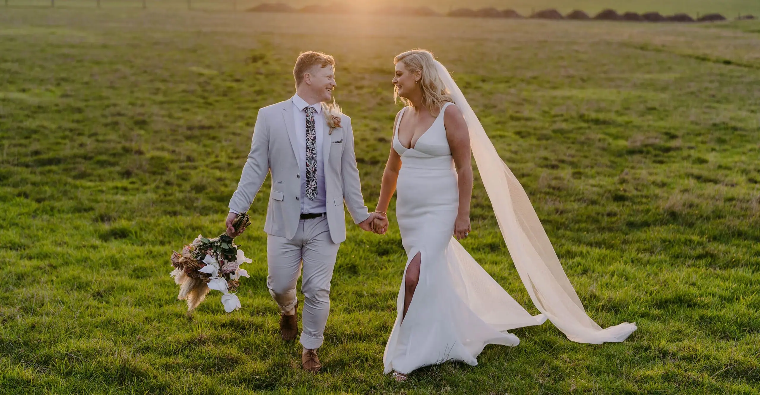 Couple walking through a green paddock with a flowing veil