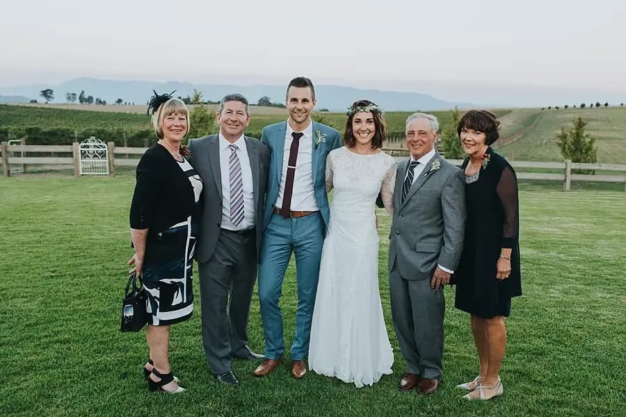 Couple posing with four guests on a green lawn overlooking distant hills.