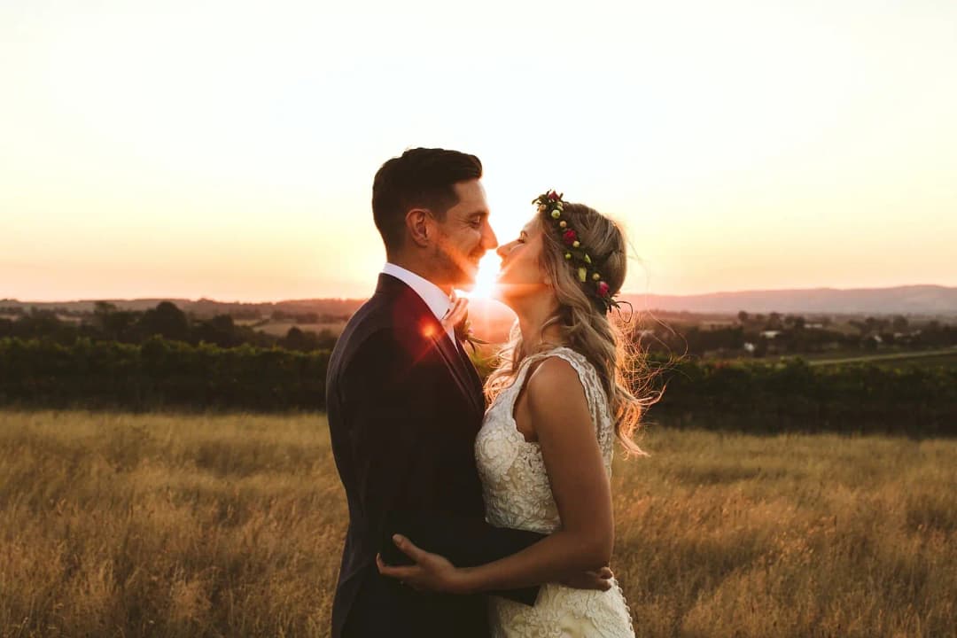 Couple embracing in a golden field with the sun between their faces.