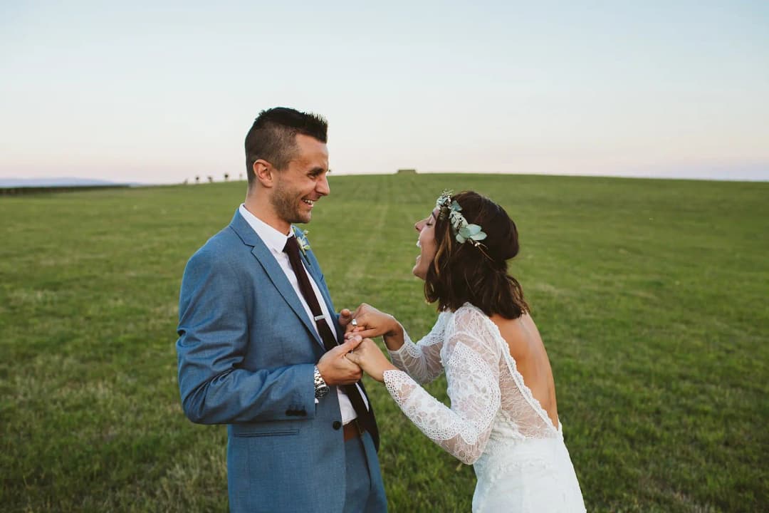 Couple holding hands and smiling in a grassy field.