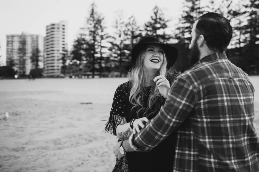 Black-and-white photograph of a woman laughing as she faces her partner on the beach.