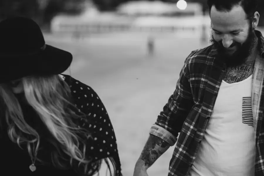 Black-and-white close-up of a couple looking down while walking hand in hand on the beach.
