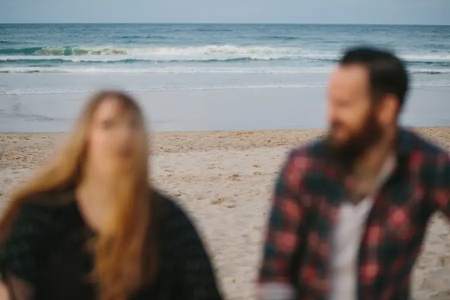 Softly blurred portrait of a couple standing together with the beach and sea behind them.