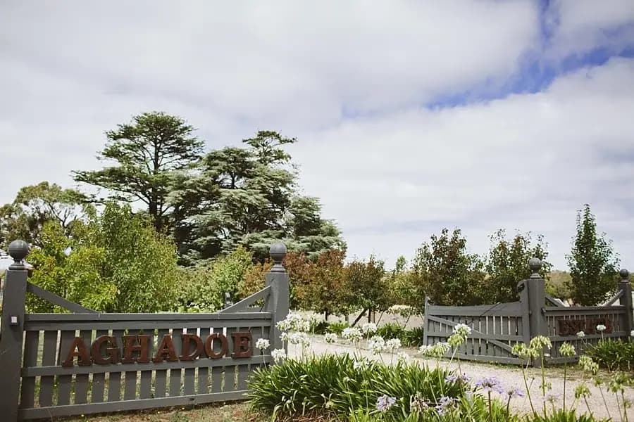 Garden entrance gate beneath trees and a cloudy sky.