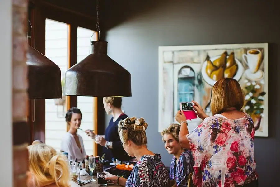 Women chat around a table while getting ready indoors.