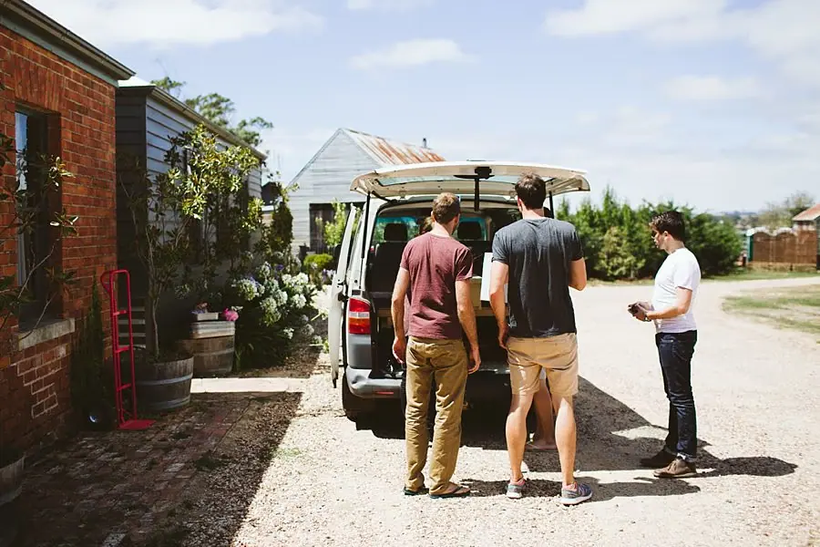 Men unload items from a van beside a brick building.