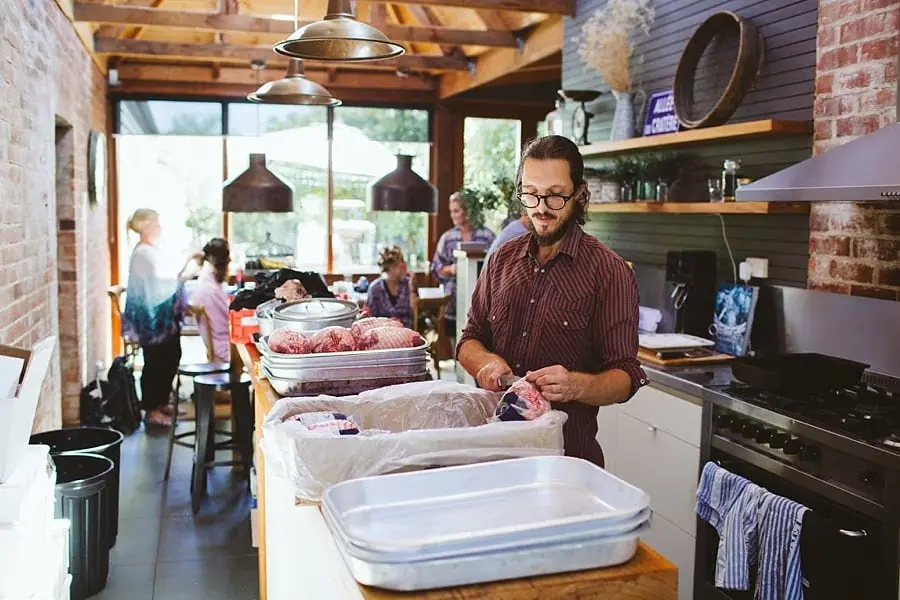 Man prepares items at a kitchen counter while guests gather behind him.