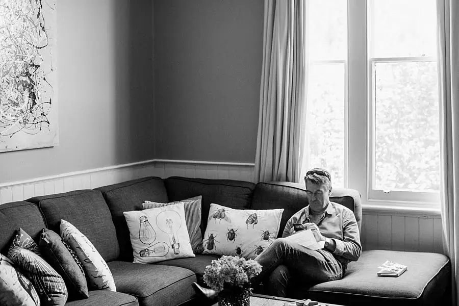 Black and white photograph of a man relaxing on a sofa beside bright windows.