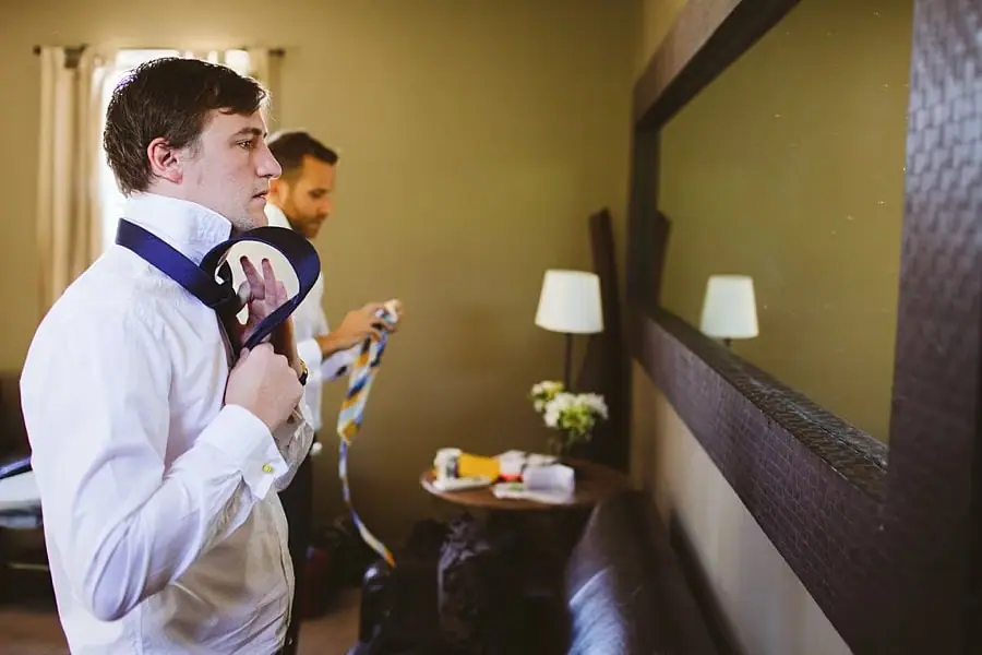 Man adjusts his tie while looking in a mirror.