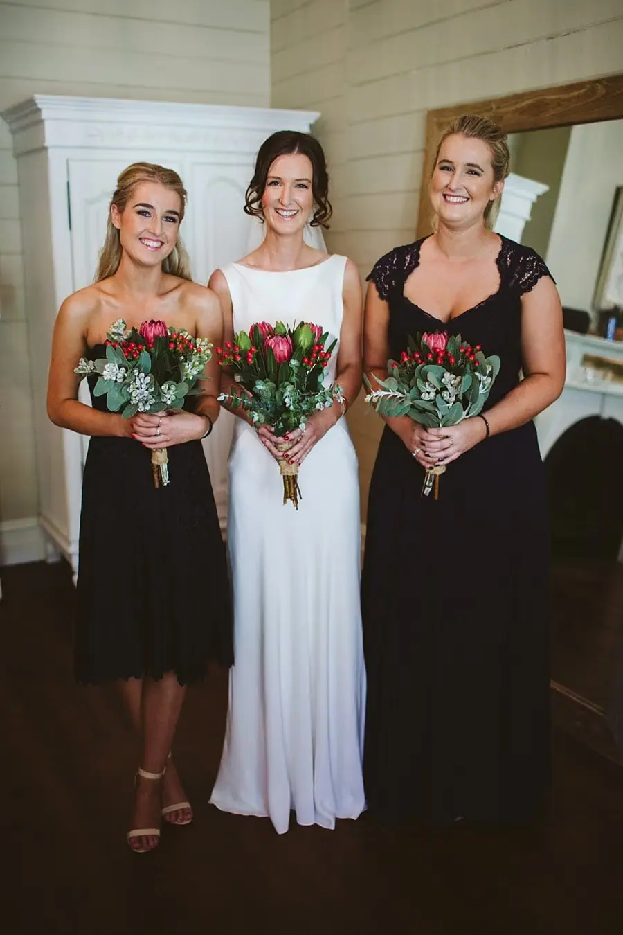 Bride poses with two bridesmaids and colourful bouquets indoors.
