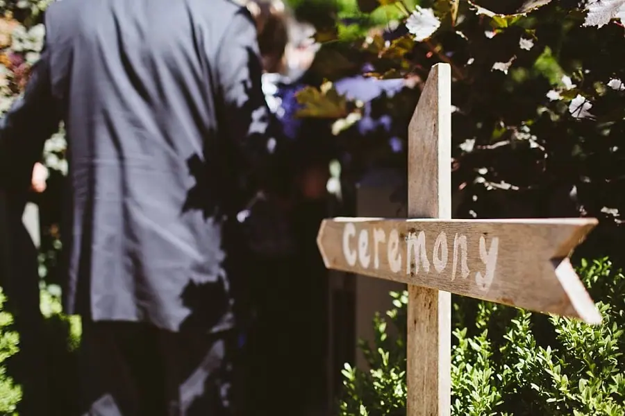 Wooden ceremony direction sign beside a garden path.