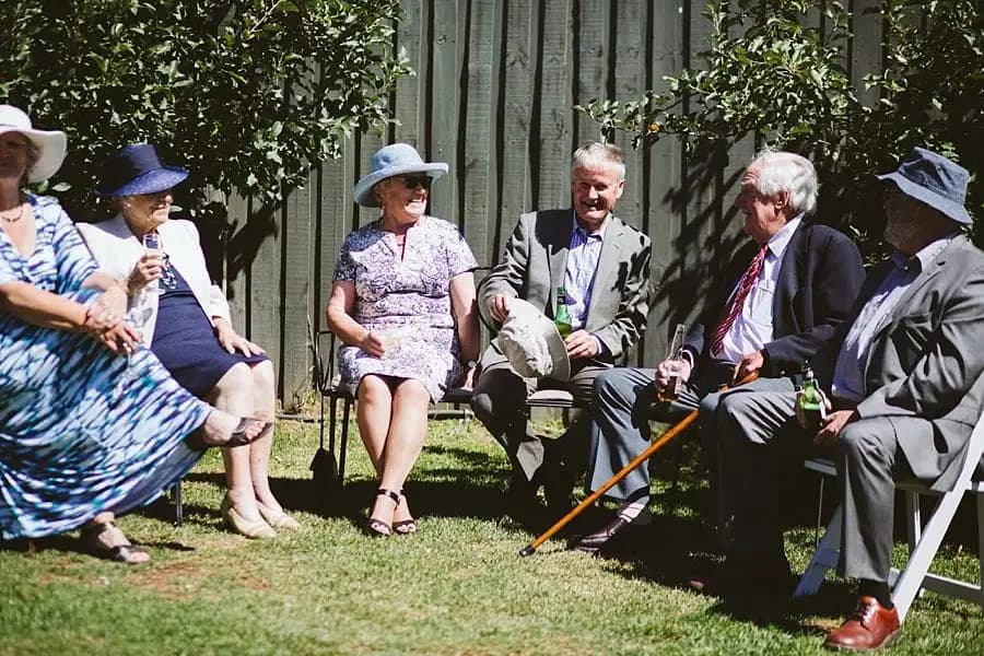 Older guests chat while seated together on the garden lawn.
