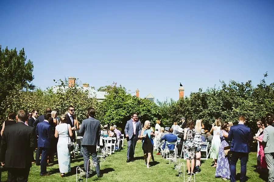 Guests gather around outdoor ceremony chairs beneath a blue sky.