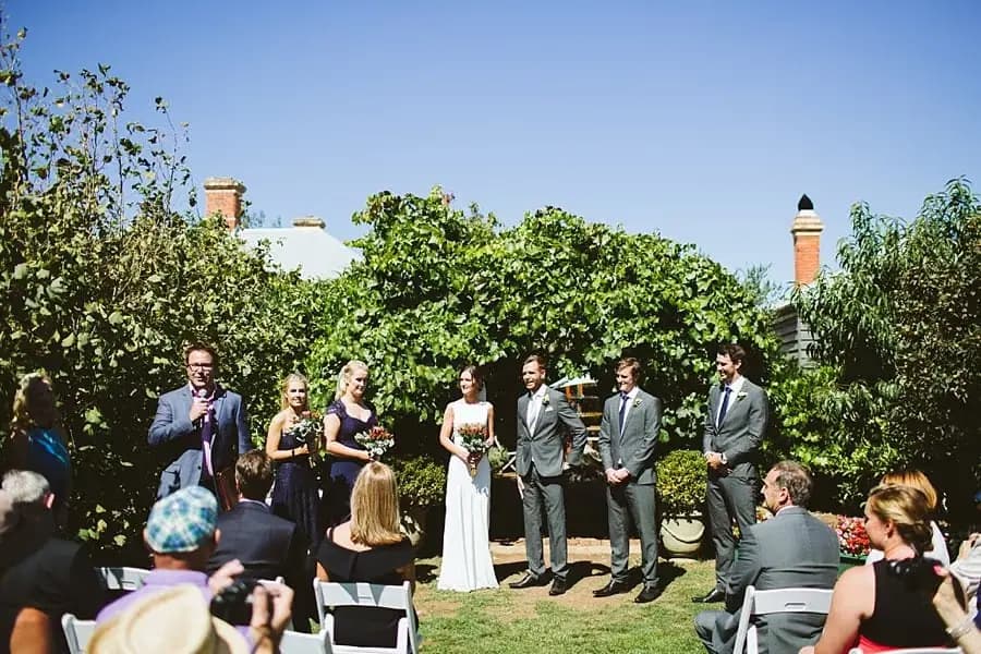 Wedding party stands before seated guests at a sunny outdoor ceremony.