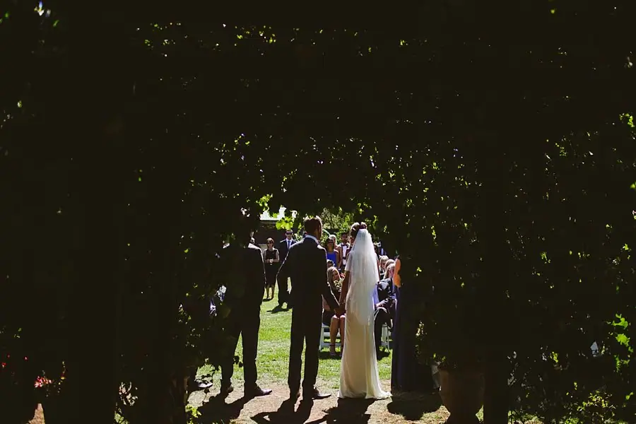 View through a leafy arch toward the couple at their ceremony.