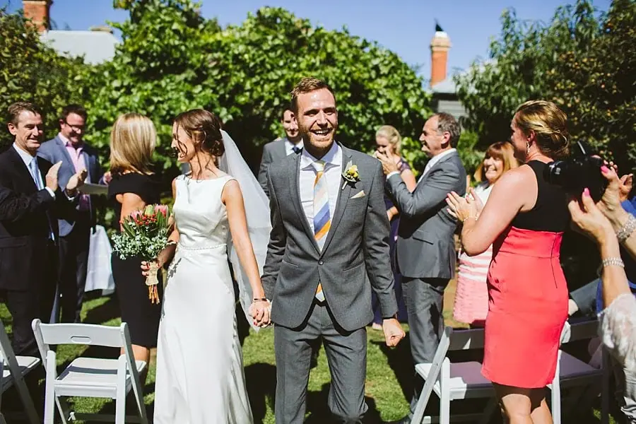 Newlyweds walk hand in hand through applauding guests.