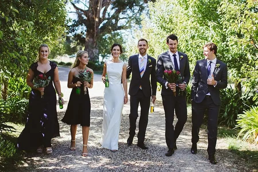 Wedding party walks together along a shaded gravel path.