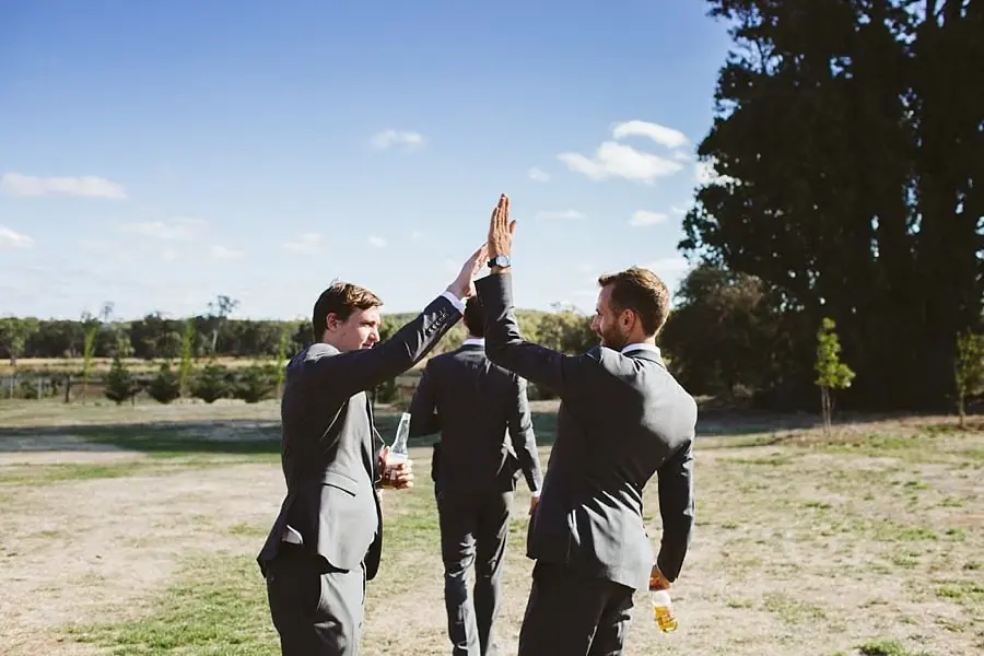 Men high-five outdoors beneath a blue sky.
