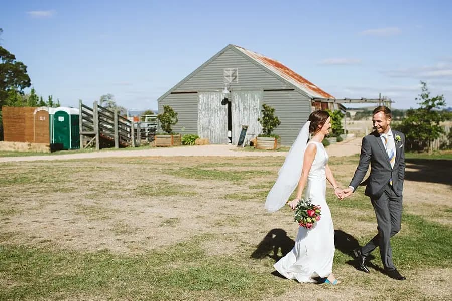 Couple walks hand in hand beside a rustic building.