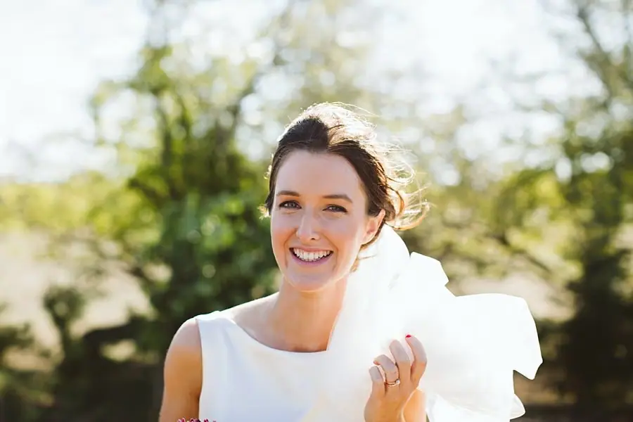 Bride smiles toward the camera while holding her veil.