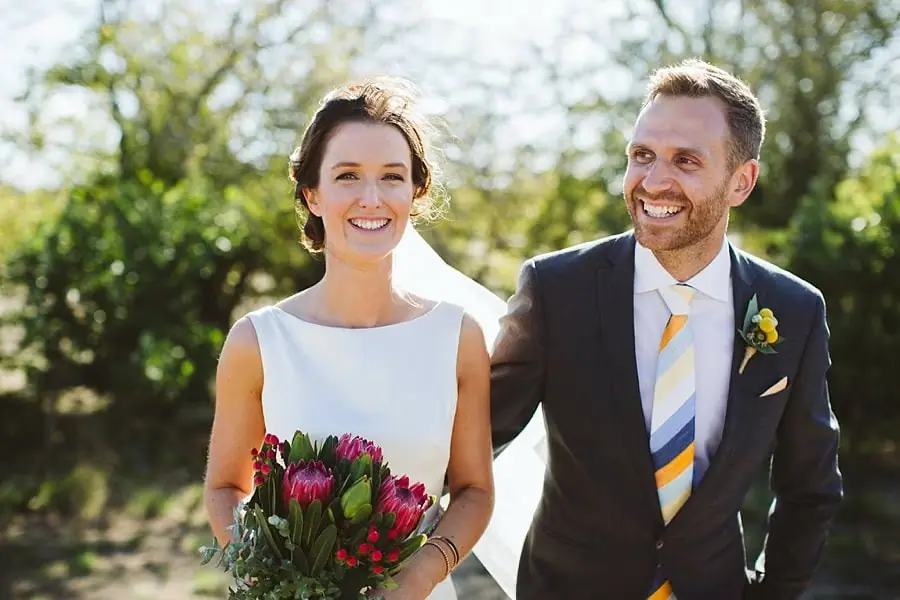 Couple laughs together outdoors with the bride holding her bouquet.