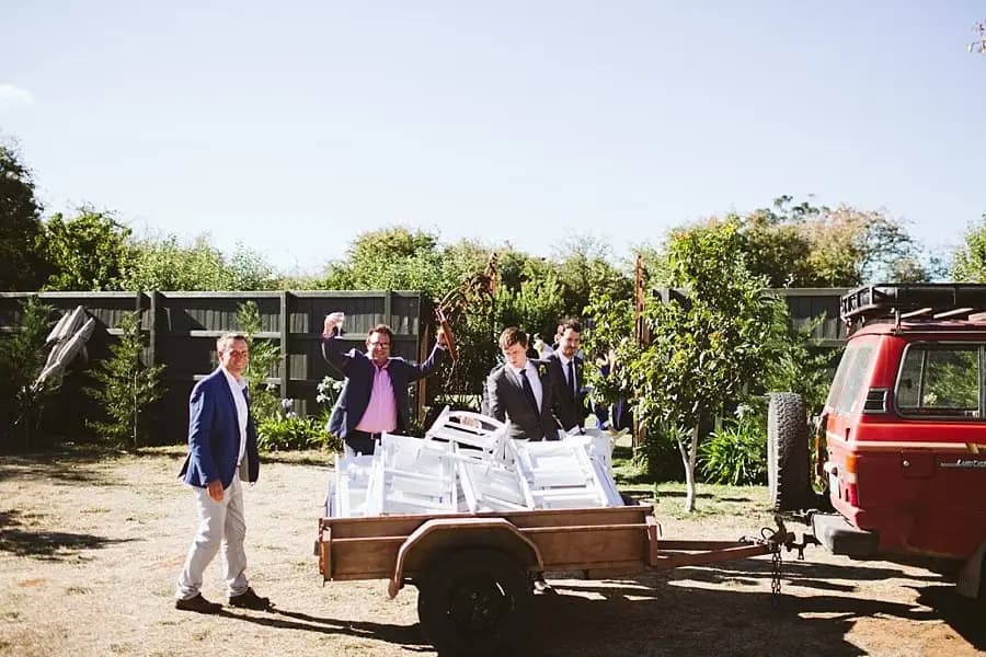 Guests stack white chairs onto a trailer beside a van.