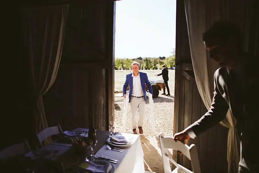 Man approaches an open barn doorway as another guest holds a chair inside.
