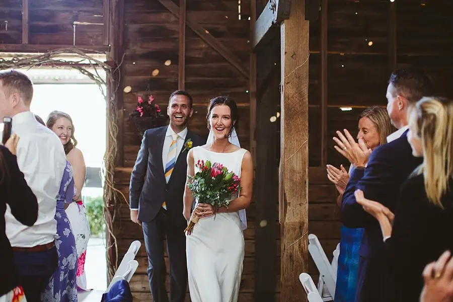 Newlyweds enter the barn as guests applaud around them.
