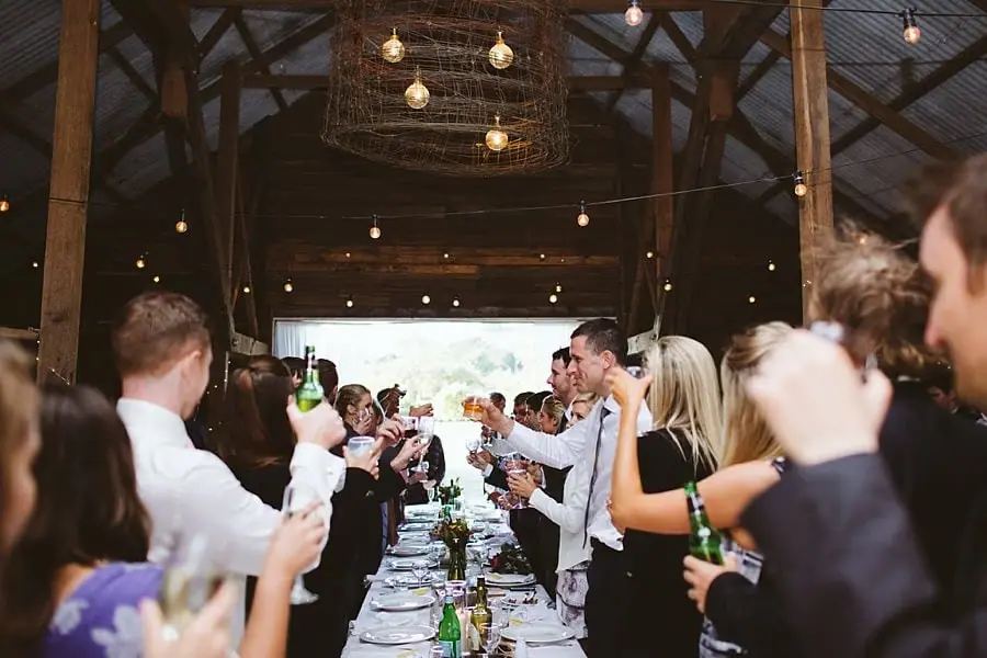 Guests raise their glasses across long reception tables inside the barn.