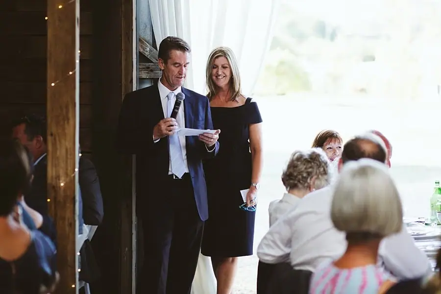 Man reads a speech into a microphone beside a woman near the open barn doorway.
