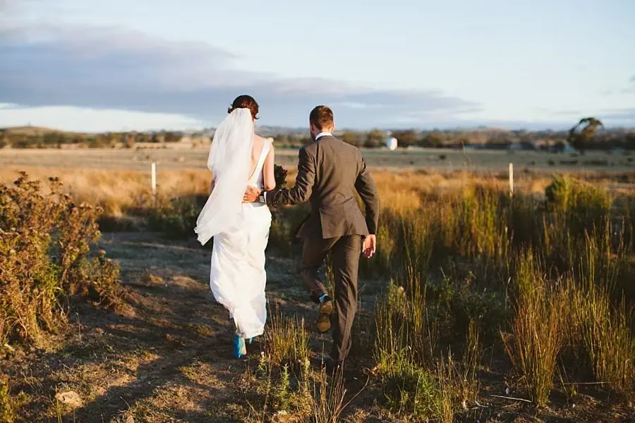 Rear view of the couple walking hand in hand through a field at sunset.