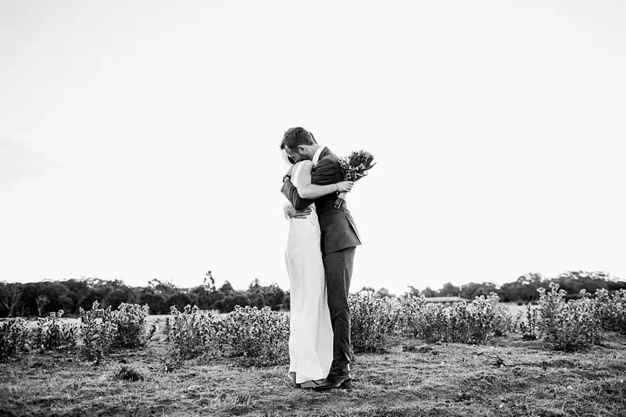 Black and white photograph of the couple embracing in a wide open field.