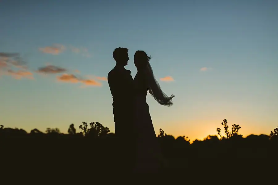 Silhouetted couple faces each other beneath a blue and orange sunset sky.