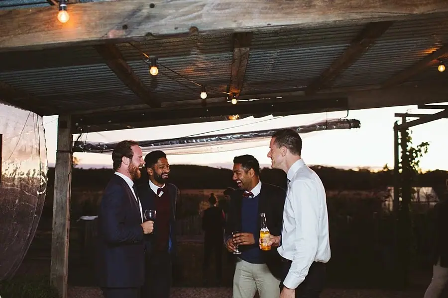 Men chat with drinks beneath the reception veranda roof.