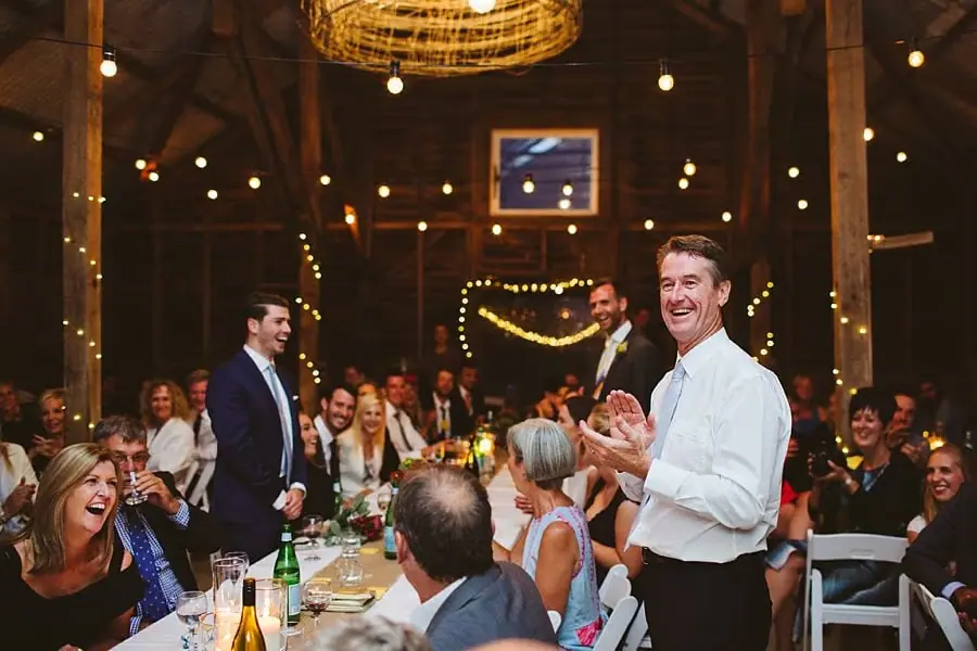 Man gives a speech beside a microphone as seated guests laugh.