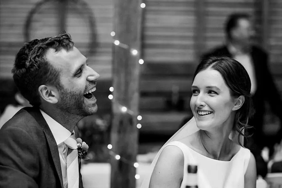Black and white photograph of the couple laughing at the reception table.