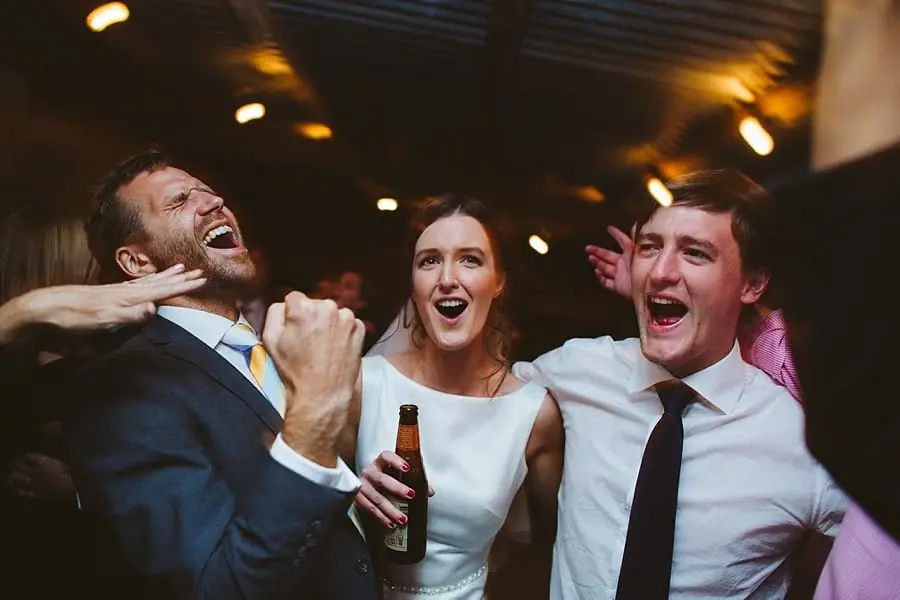 Bride, groom and a friend cheer together on the dance floor.