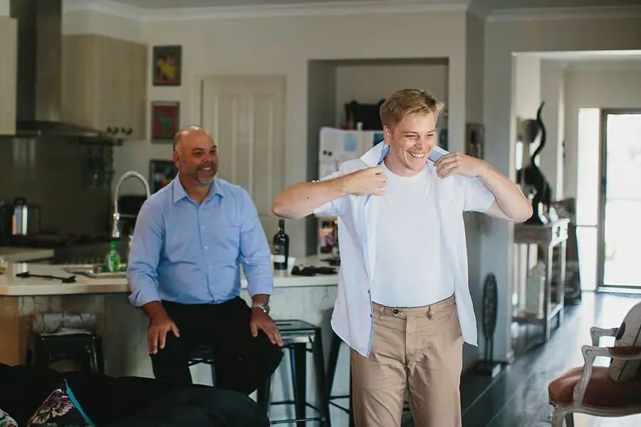 Man in a white shirt adjusting his bow tie beside a smiling companion.