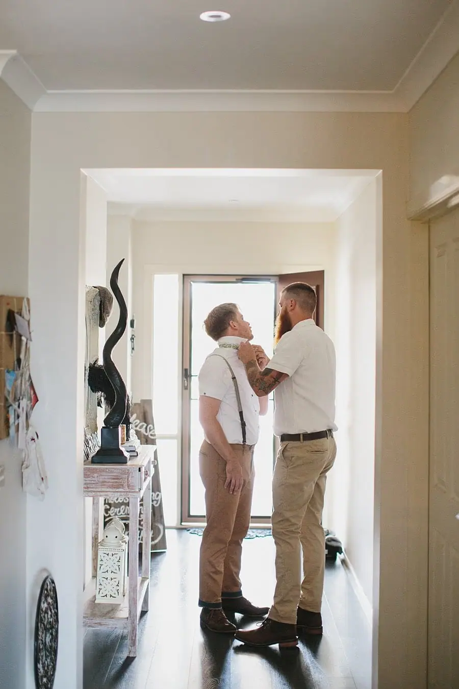 Two men adjusting clothing in a bright hallway.