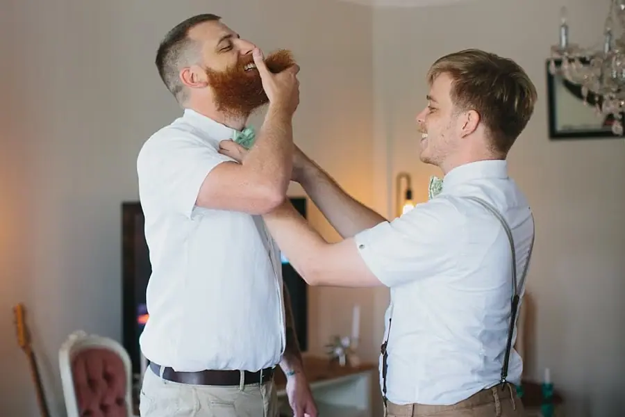 Man helping a bearded companion adjust his bow tie.