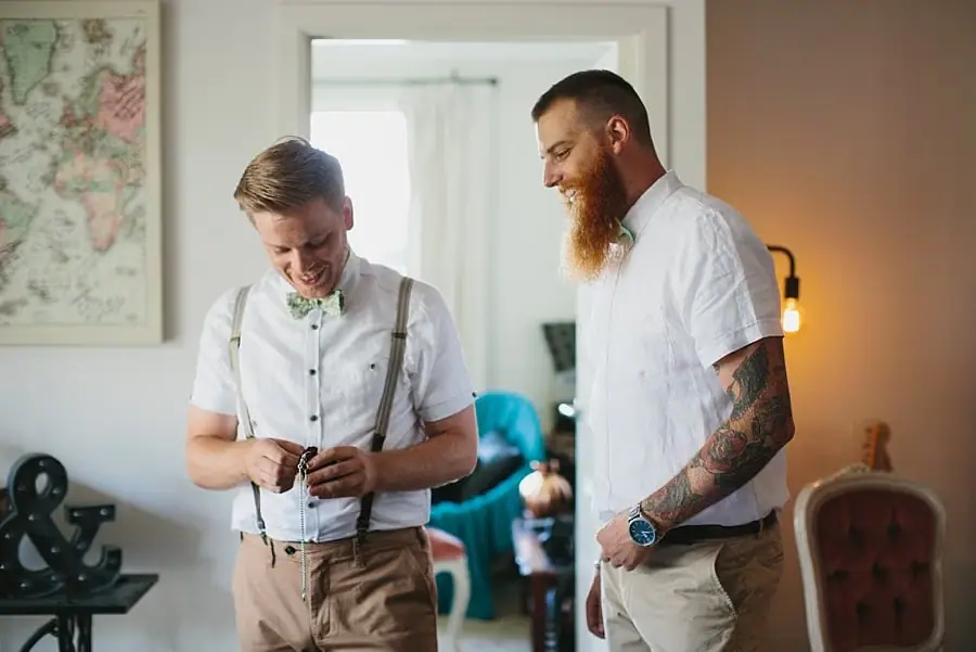 Man fastening his shirt while a bearded companion watches.