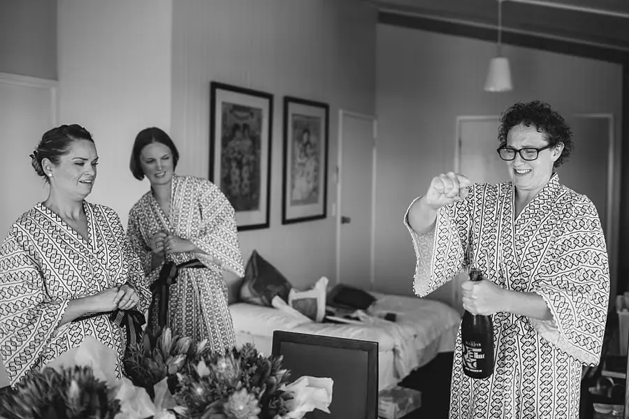 Black-and-white photograph of women laughing as one holds a bottle.