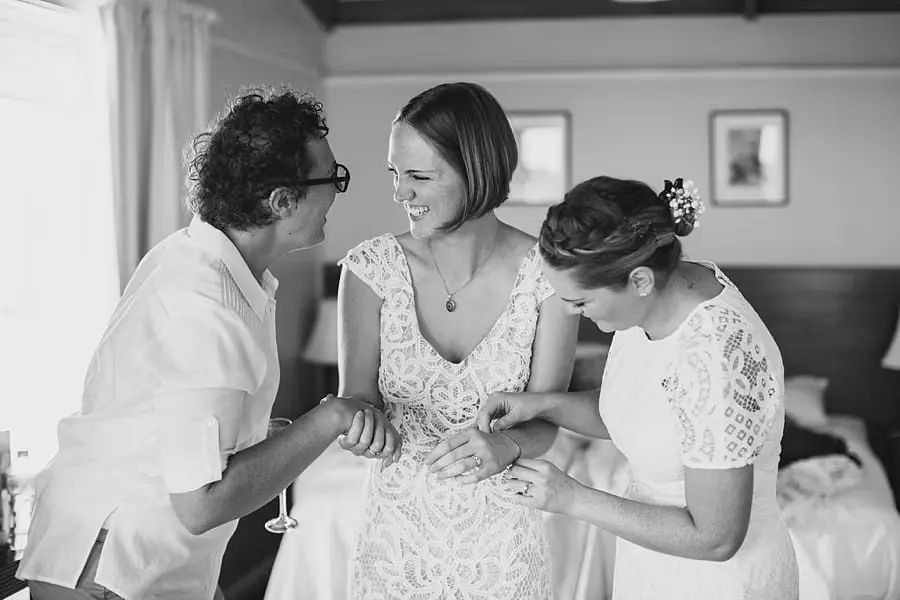 Black-and-white photograph of women smiling and adjusting the bride's dress.