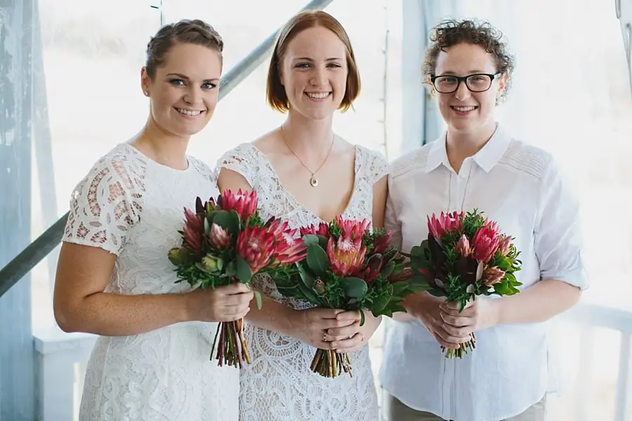 Bride standing with two companions holding bright pink flower bouquets.