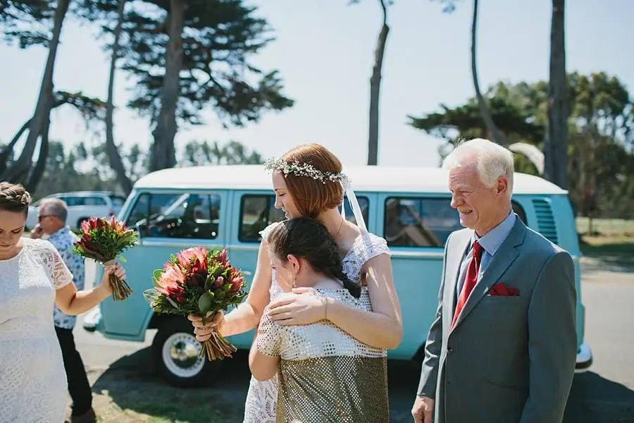 Bride greeting a woman beside a pale blue van.