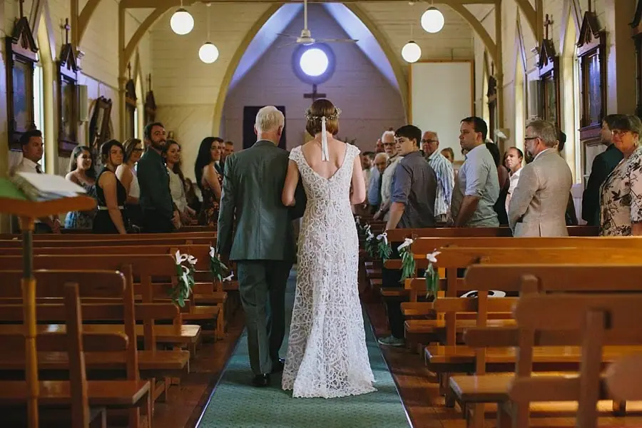 Bride walking down a church aisle alongside a suited man.